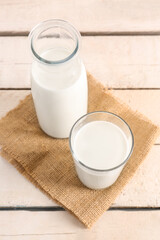 Bottle and glass with fresh milk on light wooden table