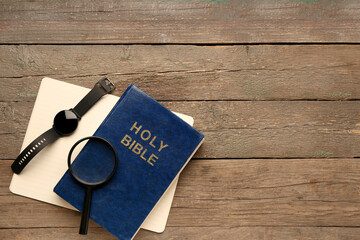 Holy Bible with magnifier, notebook and smartwatch on wooden background