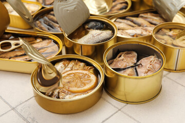 Many opened cans with different fish on tiled table, closeup