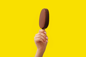 Woman holding delicious chocolate covered ice cream on stick against yellow background