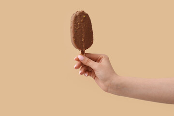 Woman holding delicious chocolate covered ice cream on stick against beige background