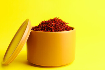 Bowl with pile of saffron on yellow background