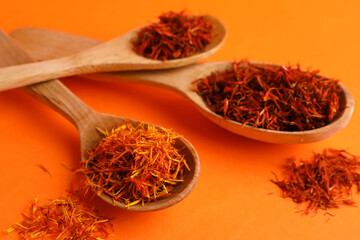 Spoons with pile of saffron on orange background