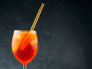 Glass of Aperol Spritz cocktail on a dark background. Cocktail Aperol Spritz with eco-friendly glass straw. Copy space