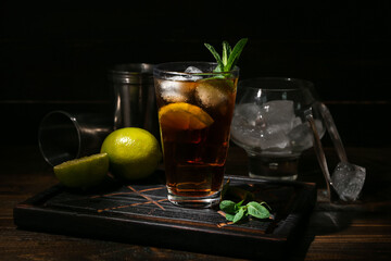Glass of tasty Cuba Libre cocktail on dark wooden background