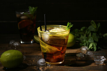 Glass of tasty Cuba Libre cocktail on dark wooden background