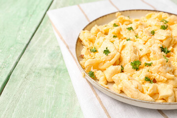Plate of scrambled eggs with napkin on green wooden background