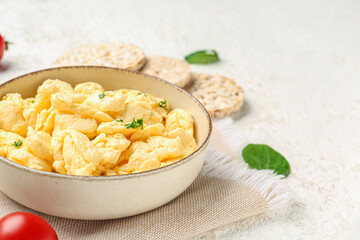 Composition with bowl of scrambled eggs and rice crackers on light background