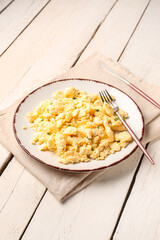 Plate of tasty scrambled eggs with cutlery on white wooden background