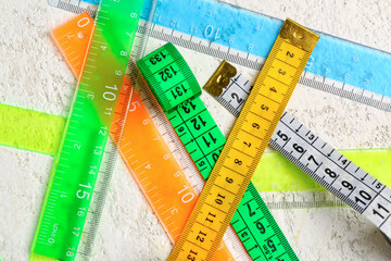 Colorful plastic rulers and measuring tapes on light grunge background