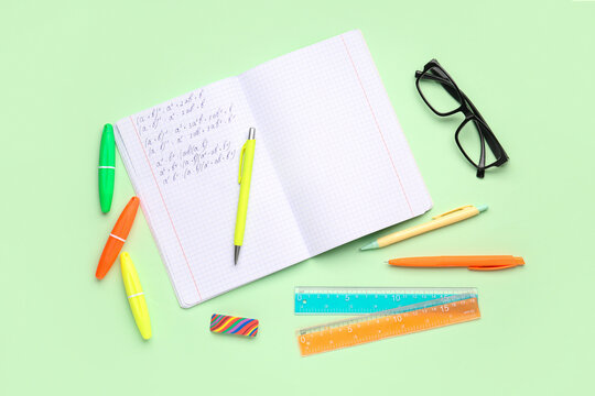 Copybook with maths formulas, glasses and stationery on green background - Powered by Adobe