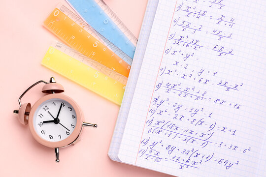 Copybook with maths formulas, alarm clock and rulers on pink background