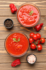 Bowls with tasty tomato sauce and fresh vegetables on wooden background