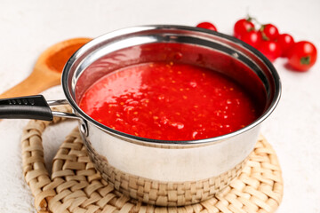 Saucepan with tasty tomato sauce on light background