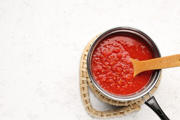 Saucepan with tasty tomato sauce on light background
