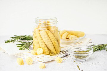 Jar with tasty canned corn cobs on light background