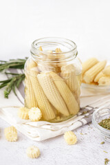 Jar with tasty canned corn cobs on light background