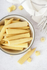 Bowl with tasty canned corn cobs on light background