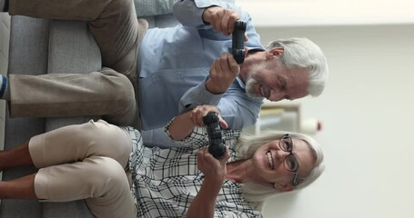 Enthusiastic mature couple sit on sofa holding controllers playing video games, spend free time using modern gadget, enjoy digital entertainment at home on carefree retirement. Hobby, Generative AI - Powered by Adobe