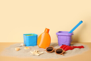 Sunscreen cream for baby with beach accessories on sand near beige wall