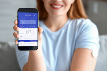 Woman with glucose sensor using mobile phone for measuring of blood sugar level at home