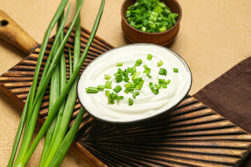 Bowl of tasty sour cream with green onion on beige background