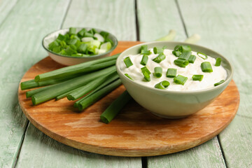 Bowl of tasty sour cream with green onion on light wooden background