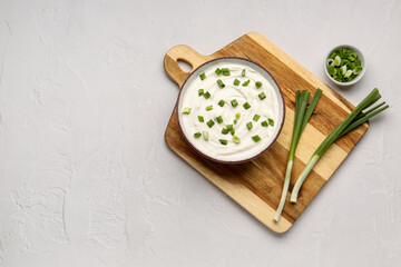 Bowl of tasty sour cream with green onion on light background