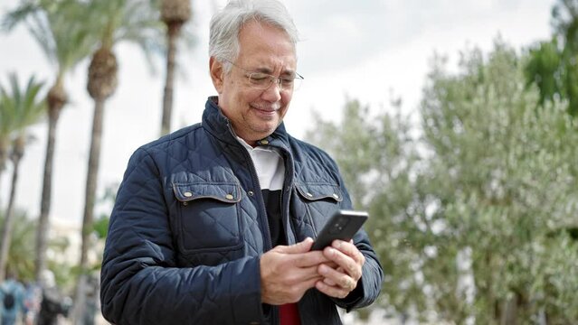 Middle age man with grey hair using smartphone smiling at park
