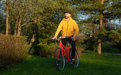 Naklejka premium Man in yellow hoodie on a red bicycle in the city park