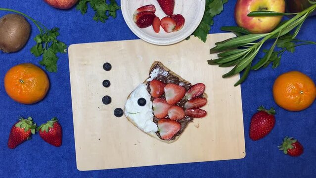 Creative kids breakfast, fish made of chocolate bread spread, strawberries and blueberries moving on the wooden board. Stop motion. High quality 4k footage