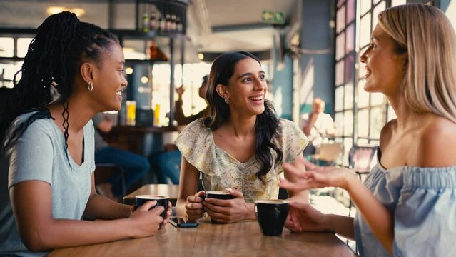 Group of multi-cultural female friends meeting in restaurant or coffee shop looking at social media on mobile phone and laughing together - shot in slow motion