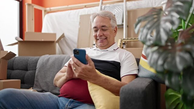 Middle age man with grey hair smiling confident using smartphone at new home