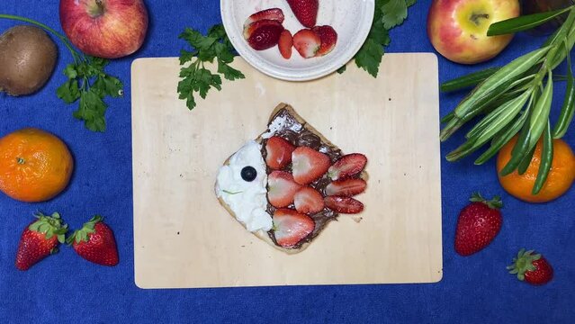 Creative kids breakfast. Fish shaped chocolate bread spread with strawberries and blueberries. Stop motion. High quality 4k footage