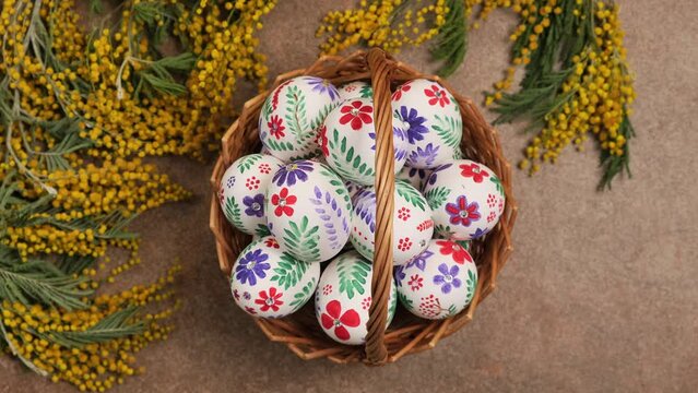 Colorful Easter eggs - traditional symbol for religious holiday. Easter eggs in the basket and mimosa flowers rotation. Happy holiday concept background  flat lay top view slow motion vertical video