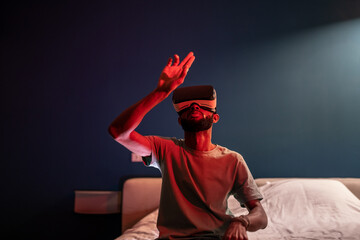 Young African American man wearing futuristic metaverse VR headset touching air with finger,...