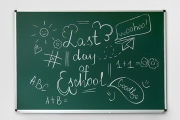 Blackboard with text LAST DAY OF SCHOOL and drawings on light wall