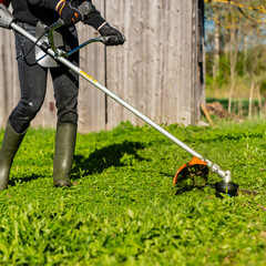 Gardener working on lawn with grass trimmer close up while wearing rubber boots on countryside