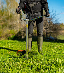 Gardener working on lawn with grass trimmer close up while wearing rubber boots on countryside