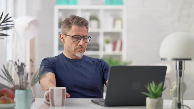 Entrepreneur managing business online with laptop computer at home. Businessman working in home office. Portrait of mature age, middle age, mid adult man in 50s browsing internet.