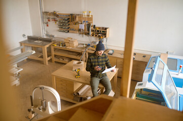 Overhead view on man carpenter sitting on table at modern joinery workshop