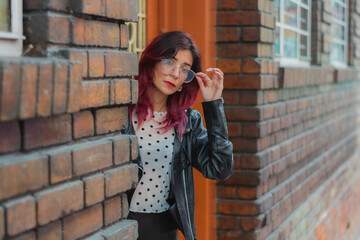 Fototapeta premium Una mujer de cabello rojo con gafas sale a la puerta a mirar hacia la calle