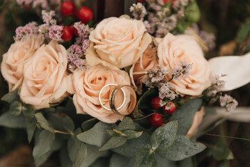 Beautiful wedding bouquet with protea and roses, wedding rings on a forest background