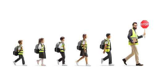 Full length profile shot of schoolchildren in reflective vests walking behind a teacher with a stop...