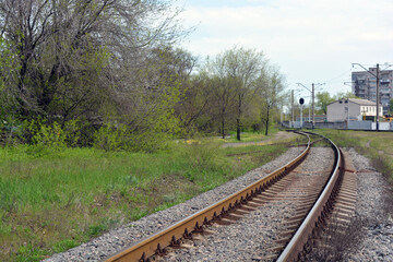 Railway track, metal lines of the railway with gray gears, green grass, large trees against the blue sky.