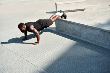 Fit sporty young black man doing push ups exercises in urban park. Strong muscular healthy African...