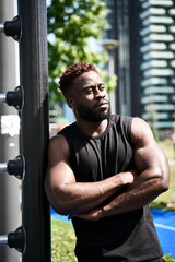 Fototapeta na wymiar Fit sporty young black man standing in workout park looking away feeling confident. Strong healthy African ethnic guy in outdoor gym resting after doing sport fitness exercises, vertical.