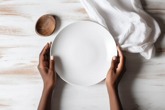 Afro-american woman's hands holding white empty plate over the tabe, textile napkin, small wooden bowl, top view. Generative AI