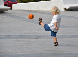 Little boy playing football on the empty street.