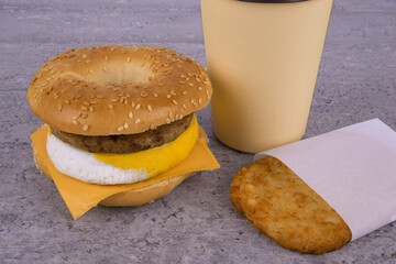 Breakfast sandwich with coffee and hash brown on concrete table. Bagle, egg, cheese and sausage. - 597889570